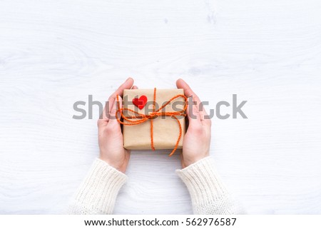 Girl holding a gift in their hands. Box with surprise on the wooden background. A gift for the holidays. Love story. Surprise. Present for Valentine\'s Day