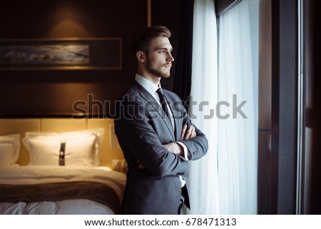 Young handsome man relaxing at his apartment in a hotel after business meeting. Business trip. Booking hotel during your vacation. Businessman in luxury room  of the expensive beautiful hotel.