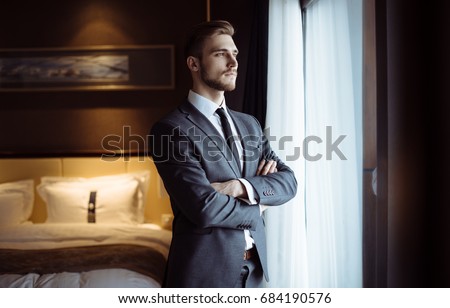 Young handsome man relaxing at his apartment in a hotel after business meeting. Business trip. Booking hotel during your vacation. Businessman in luxury room  of the expensive beautiful hotel.