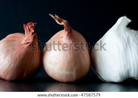 two shallot bulbs and one garlic bulb against dark background