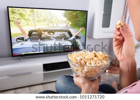 Close-up Of A Person\'s Hand Holding Popcorn While Movie Plays On Television At Home
