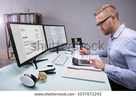 Side View Of A Young Businessman Calculating Invoice With Calculator At Workplace