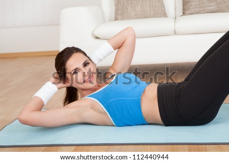 Attractive happy woman lying on a mat working out doing lift ups to strengthen her abdominal muscles