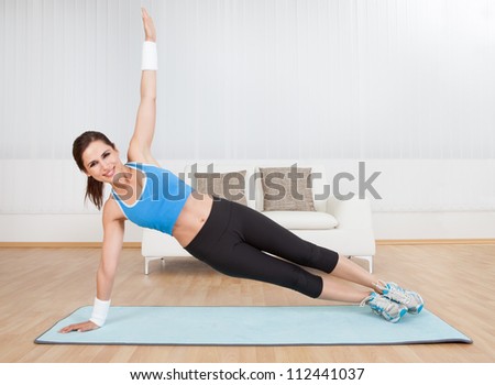 Smiling fit woman practising yoga balancing on one arm with her body raised off the floor in a health and fitness concept