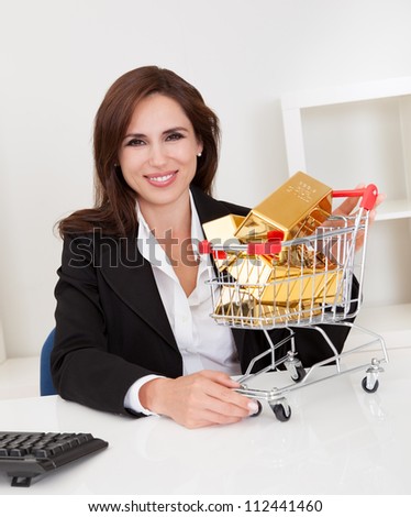 Portrait of beautiful young businesswoman presenting gold bars in mini shopping cart