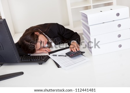 Frustrated businesswoman with stack of folders on computer desk