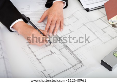 Midsection of female architect with model house, blueprints and spirit level on office desk