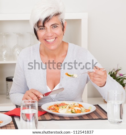 Attractive senior woman sitting at a table eating a meal in living room