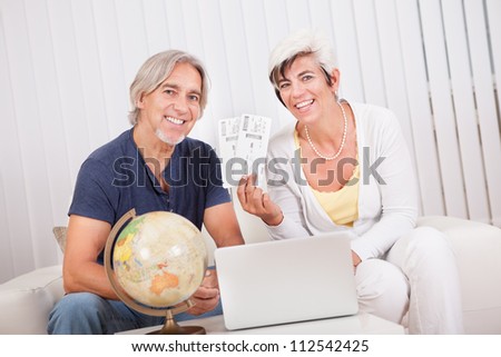 Ecstatic senior couple giving a thumbs up of success and victory as they display the tickets for their vacation