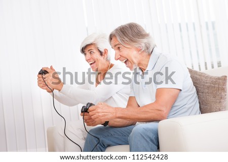 Excited middle-aged couple sitting on a sofa in their living room in front of the television screen playing computer games