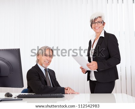 A senior business executive seated at his desk and his secretary or personal assistant