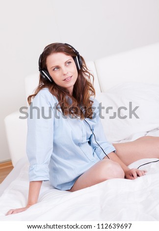 Woman relaxing on her bed in a casual blue shirt wearing stereo headphones bed listening to music