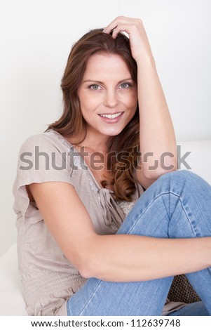 Casual barefoot woman in jeans sitting on a couch in her living room with a cheerful smile