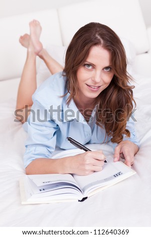 Attractive you woman lying relaxing on a sleeper couch writing in her diary