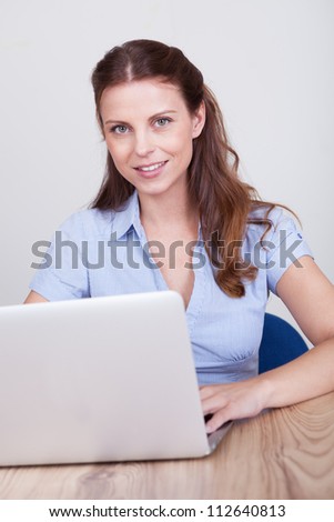 Friendly smiling woman sitting at a wooden table working at a laptop
