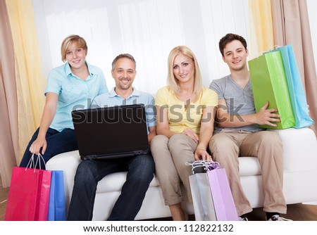 Happy family of online shoppers laden with gifts sitting around the father who is sitting with his laptop computer on his lap