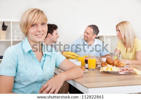 Attractive teenage girl sitting in the foreground with her family seated at the table in front of a large healthy breakfast