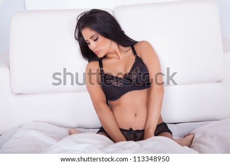 Beautiful sexy woman in black lingerie lying on her stomach on her bed with her feet in the air