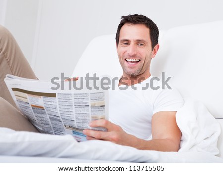 Young Man Holding Cup In Hand Reading Newspaper, Indoors
