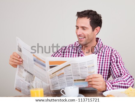 Portrait Of Young Man Reading Newspaper At Breakfast, Indoors