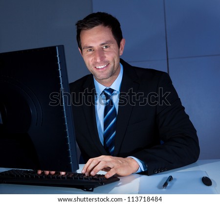 Portrait Of Happy Businessman Using Computer At Workplace