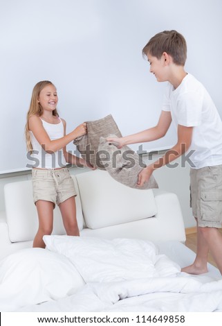Siblings Having A Pillow Fight Together On Bed In Bedroom
