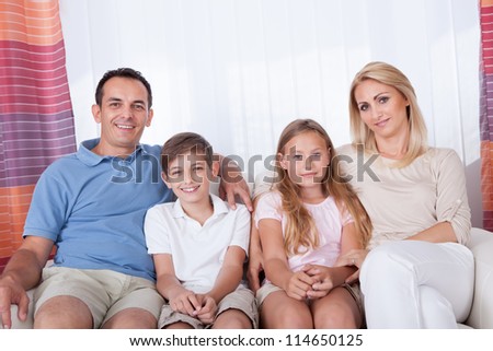 A Happy Family With Two Children Sitting On Sofa At Home