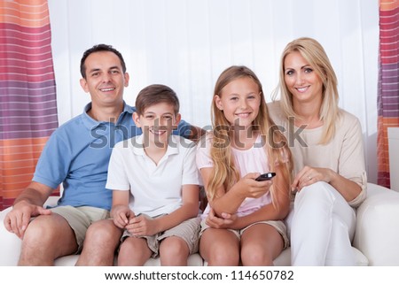 A Happy Family With Two Children Sitting On A Sofa Watching Tv At Home