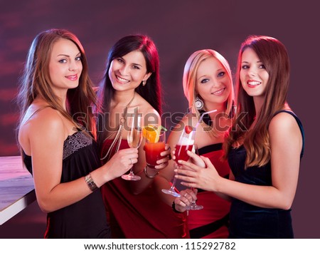 Group of four happy beautiful young female friends celebrating in a nightclub with glasses of cocktail in their hands