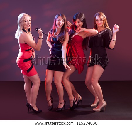 Group of glamorous young women in evening attire dancing together at a nightclub or disco