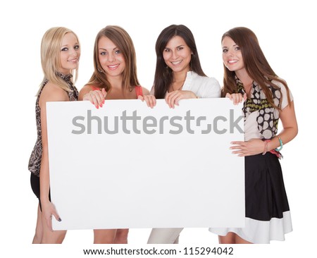 Four attractive smiling young women with a blank white sign with copyspace for your text