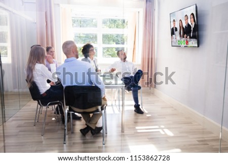 Group Of Diverse Businesspeople Looking At Television While Video Conferencing In Boardroom