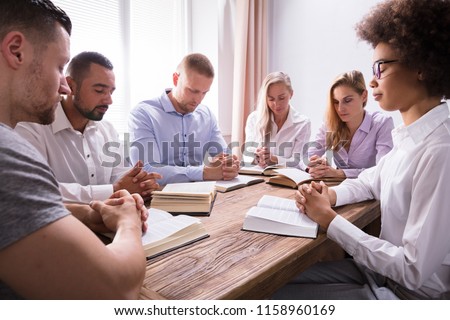 Group Of Young Multiethnic People Reading Bible Over Wooden Desk