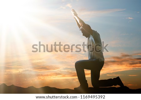 Side View Of A Man Kneeling And Praying Against Cloudy Sky At Sunset
