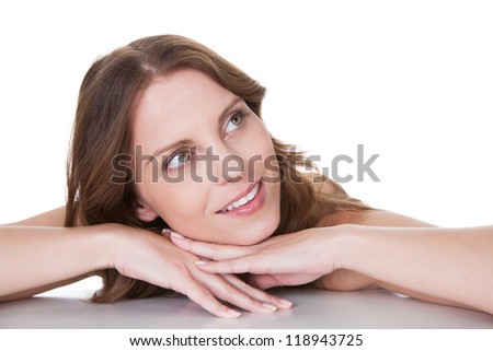 Happy woman leaning forwards on a table with her chin on her hands daydreaming as she stares up to heaven