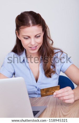 Young woman seated at her laptop entering her credit card details while shopping online
