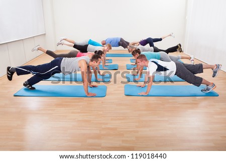 Large class of diverse people working out in a gym together on blue mats doing leg ups in a health and fitness concept