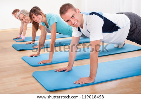 Group of diverse healthy people in a gym class doing press ups while exercising on two rows of blue mats on a wooden floor