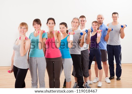 Aerobics class of diverse men and women of different ages working out in a gym with dumbbells flexing their arm muscles