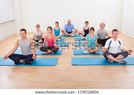 Diverse group of people practicing yoga in a gym sitting cross-legged on their mats meditating