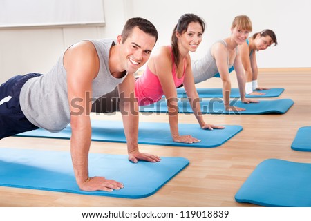 Group of diverse healthy people in a gym class doing press ups while exercising on two rows of blue mats on a wooden floor