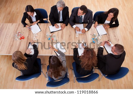 Overhead view of a group of professional business people in a meeting seated around a wooden table with their notepads