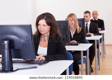 Group of diverse business people working in a support centre sitting at desks in front of computer monitors responding to email enquires