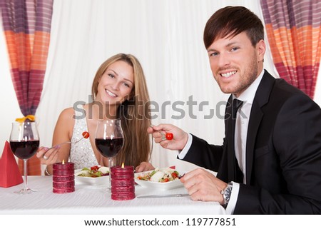 Young couple seated at a restaurant table enjoying a romantic dinner by candlelight and drinking red wine
