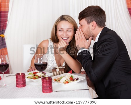 Romantic lovers sitting at an elegant restaurant table enjoying a meal and sharing secrets whispering to each other