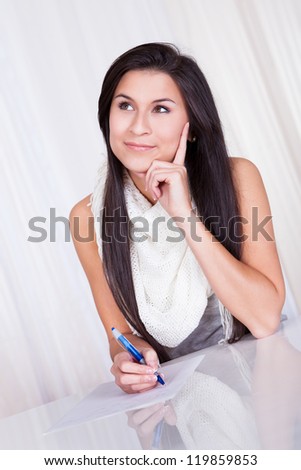 Beautiful woman sitting at a table smiling happily and writing notes on a sheet of paper