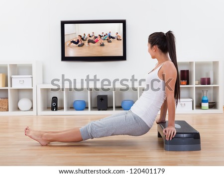 Side view of an athletic barefoot young woman doing exercises in her living room while watching program or tape on television