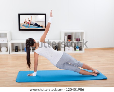 Woman practicing yoga at home standing on a mat on her living room floor while watching and participating in a class