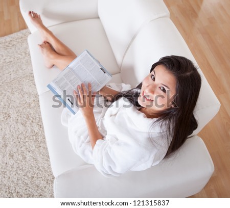Attractive woman with a lovely serene expression sitting on a couch reading a book in a white gown