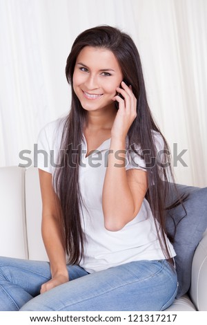 Attractive woman with long straight brunette hair smiling at the camera and talking on her mobile phone